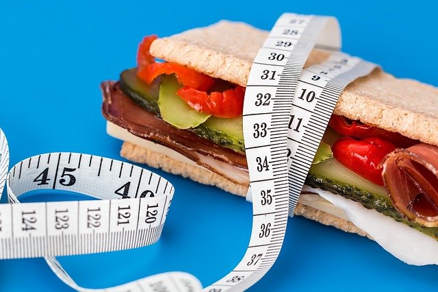 A picture of a sandwich being measured with a measuring tape to convey irony about calorie counting 