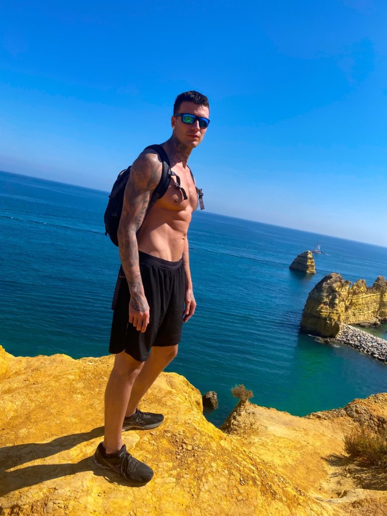 Jakob Roze exploring the cliffs of the Algarve region in Portugal with his shirt off and abs showing. 