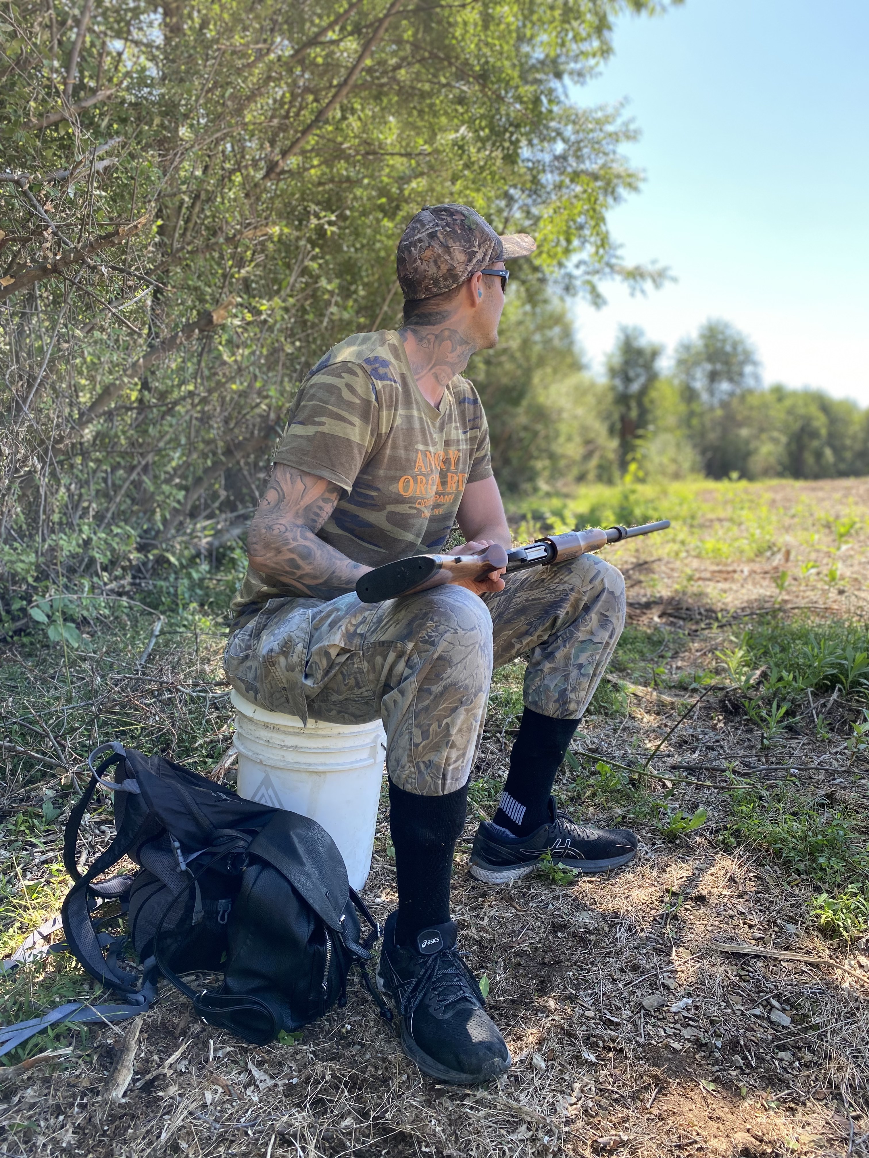 Jakob Roze hunting doves outdoors. He is sitting on a bucket with a gun looking for doves to fly by