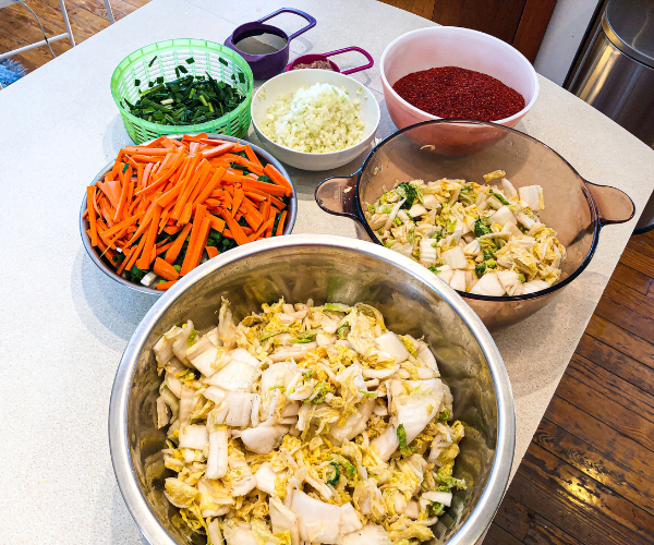 Kimchi ingredients spread out on a table including cabbage, carrots, radish, onion, garlic, fish sauce