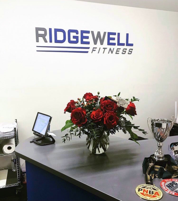 A picture of the gym Ridgewell Fitness and a vase of red roses sitting on the front desk