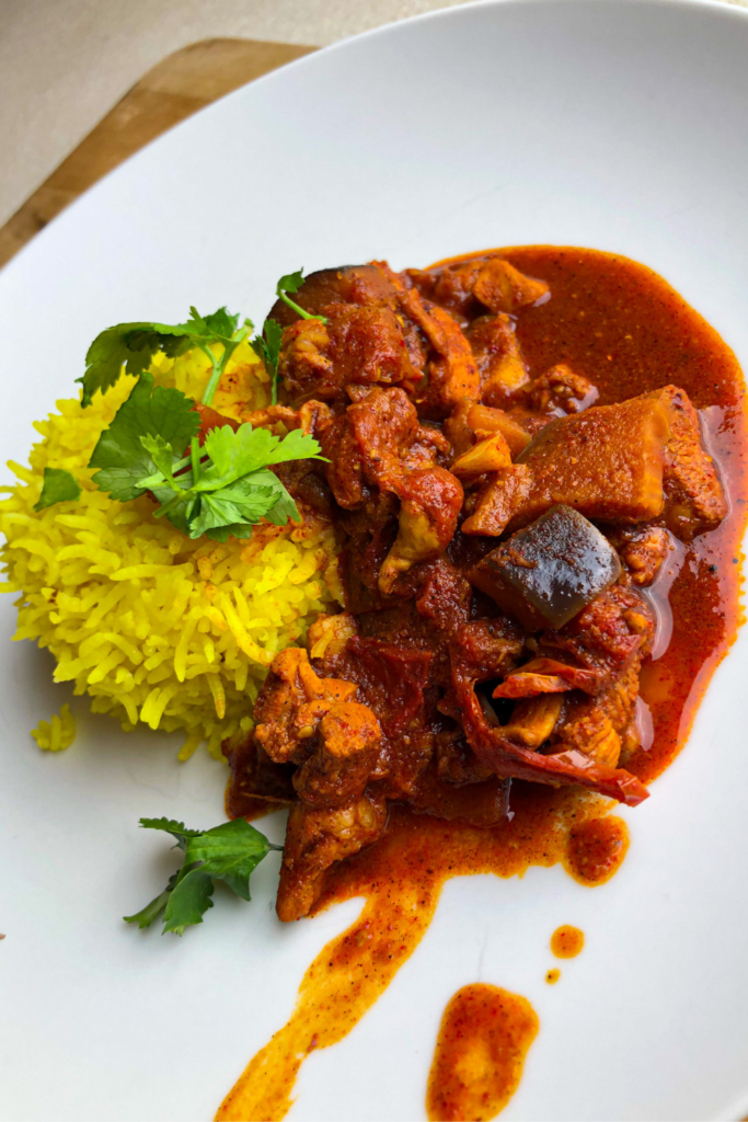 A picture of heavily spices Chicken Vindaloo and half a cup of rice on a plate