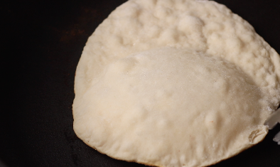 Flatbread in a pan on the stove beginning to rise as shown by the bubbles. 