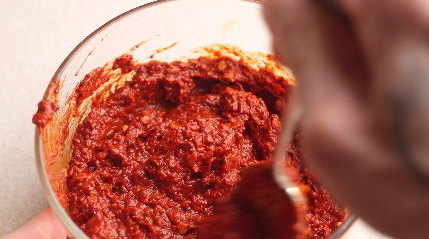 Bright red harissa sauce in a bowl being mixed with a spoon. 