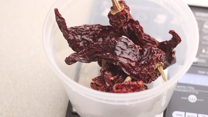 Red Kashmiri whole dried peppers being weighed on a scale