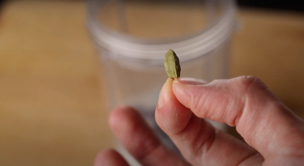 A cardamom pod being held up 