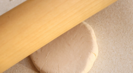 Flatbread dough being rolled flat with a rolling pin.