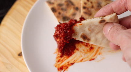A piece of flatbread dipped into the harissa sauce.
