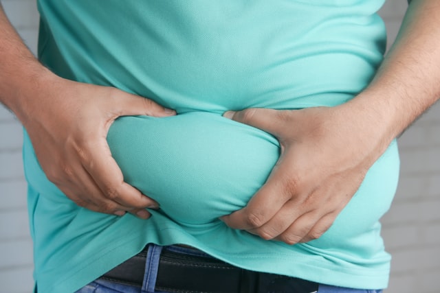 A picture of a person with abdominal obesity holding their stomach.