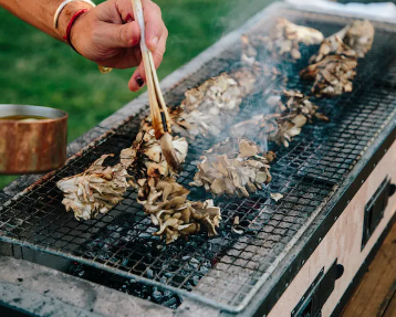 A layer of wild foraged mushrooms being basted on a grill.