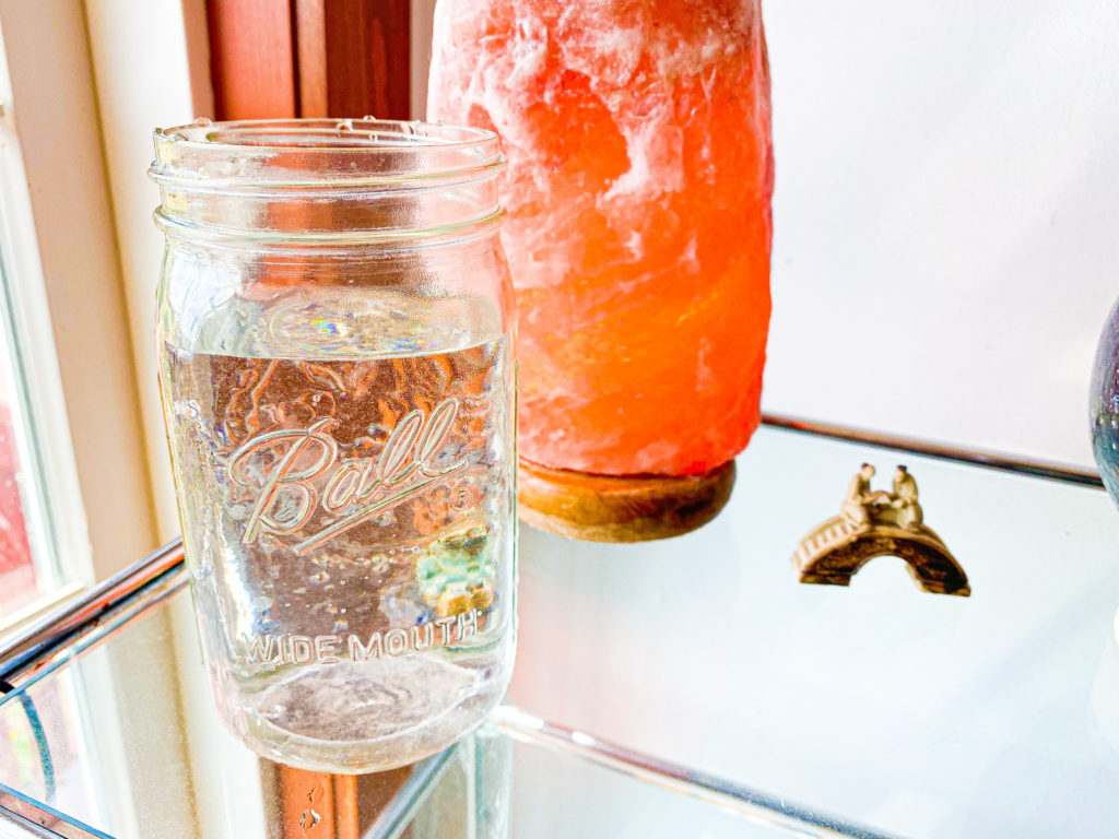 A mason jar filled with water sitting next to a pink salt lamp.