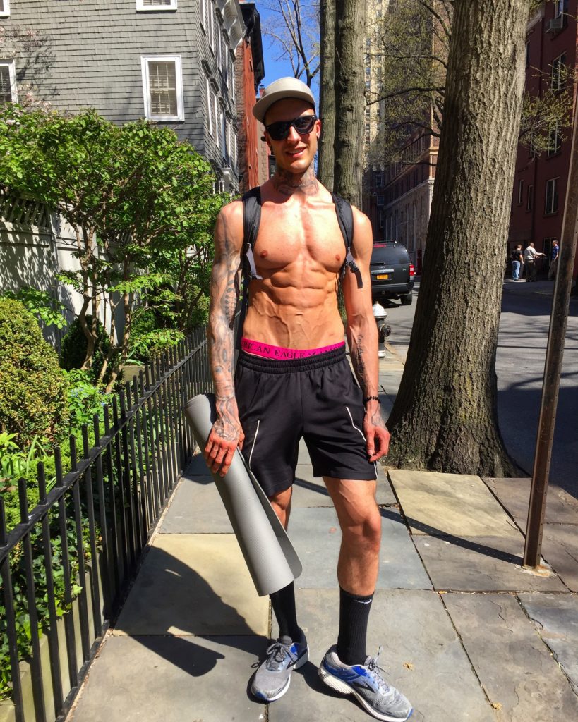 Jakob Roze showing his lean physique, holding an exercise mat. 