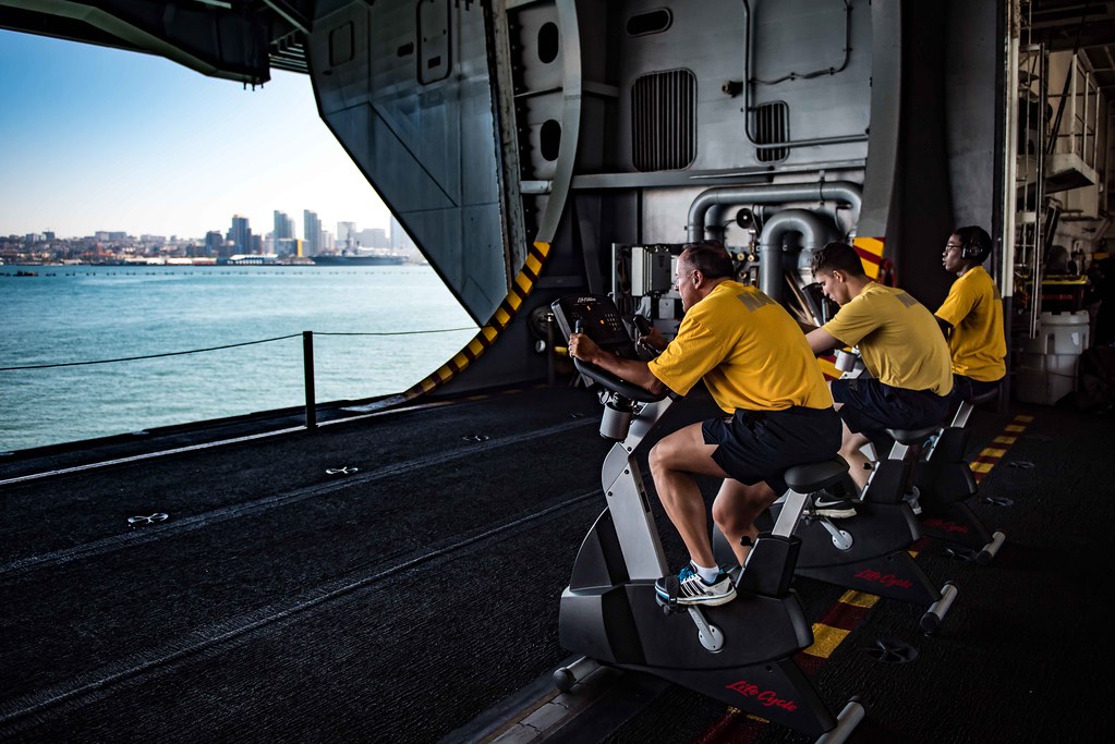 A group of men doing cardio on stationary bikes overlooking the water.