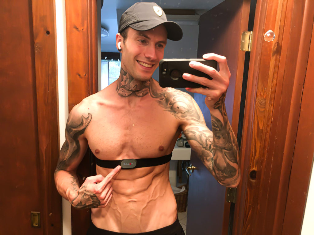 Jakob Roze pointing to a chest strap heart rate monitor in the mirror with his shirt off.