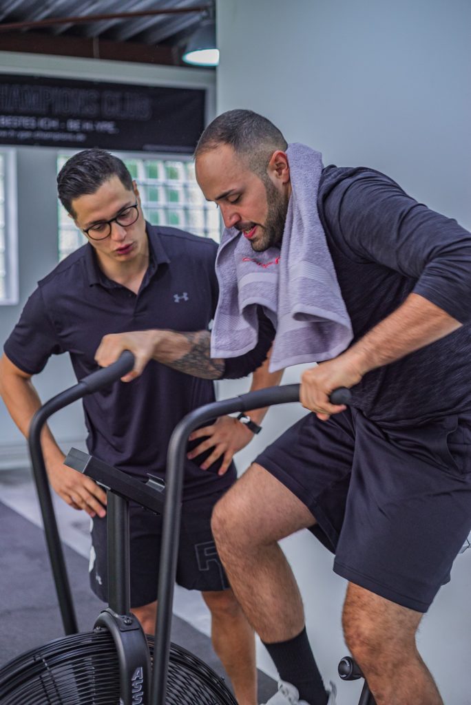 A trainer coaching a guy on a stationary exercise bike.