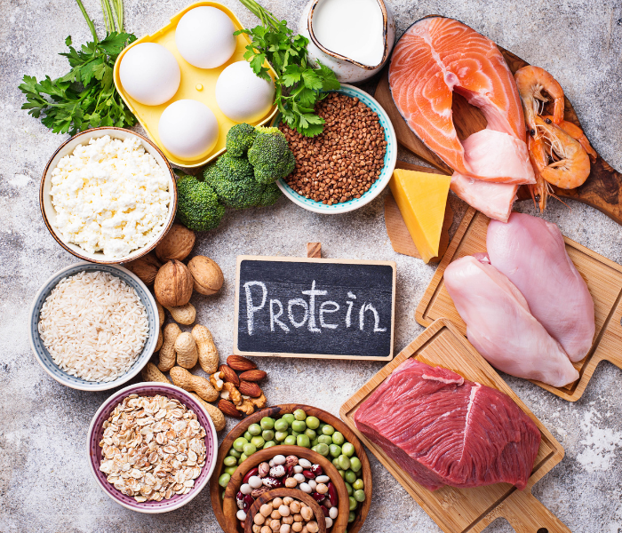 A variety of protein sources arranged nicely on a surface with a sign that says "protein"