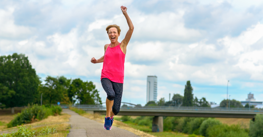 A middle-aged woman jumping in the air with a big smile on her face.