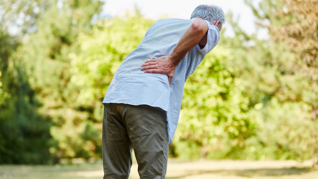 An older man holding his back in pain.