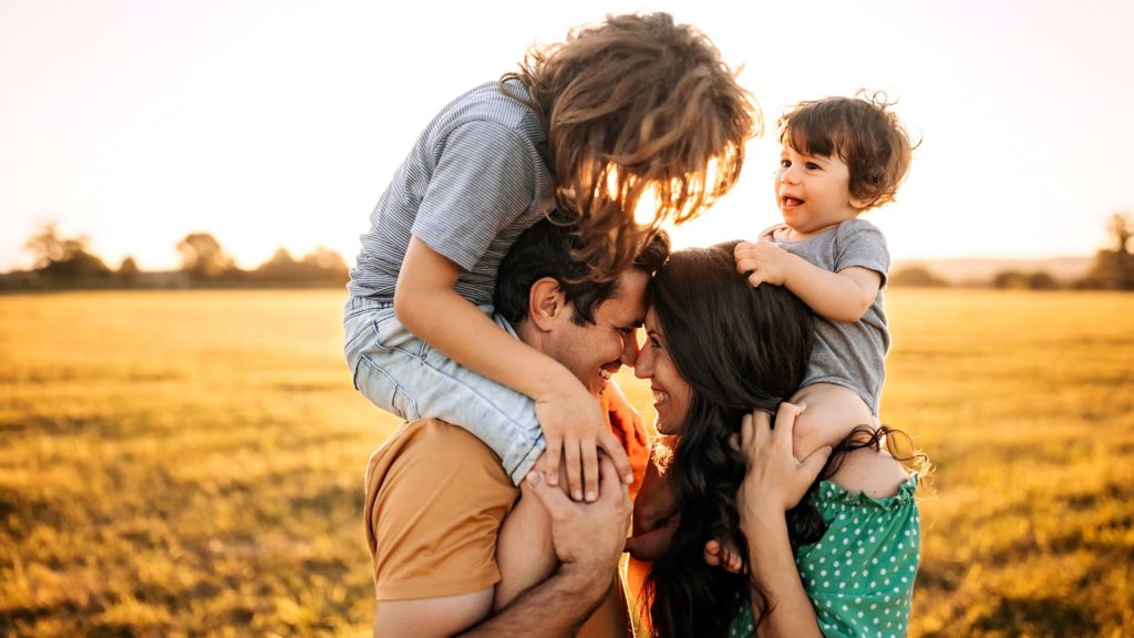 Two parents with their children on their shoulders smiling at each other.