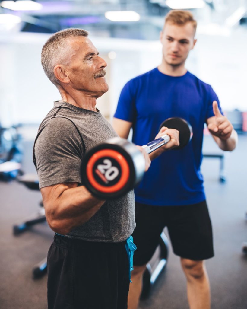 A personal trainer training a middle-aged man in the gym (lifting weights).