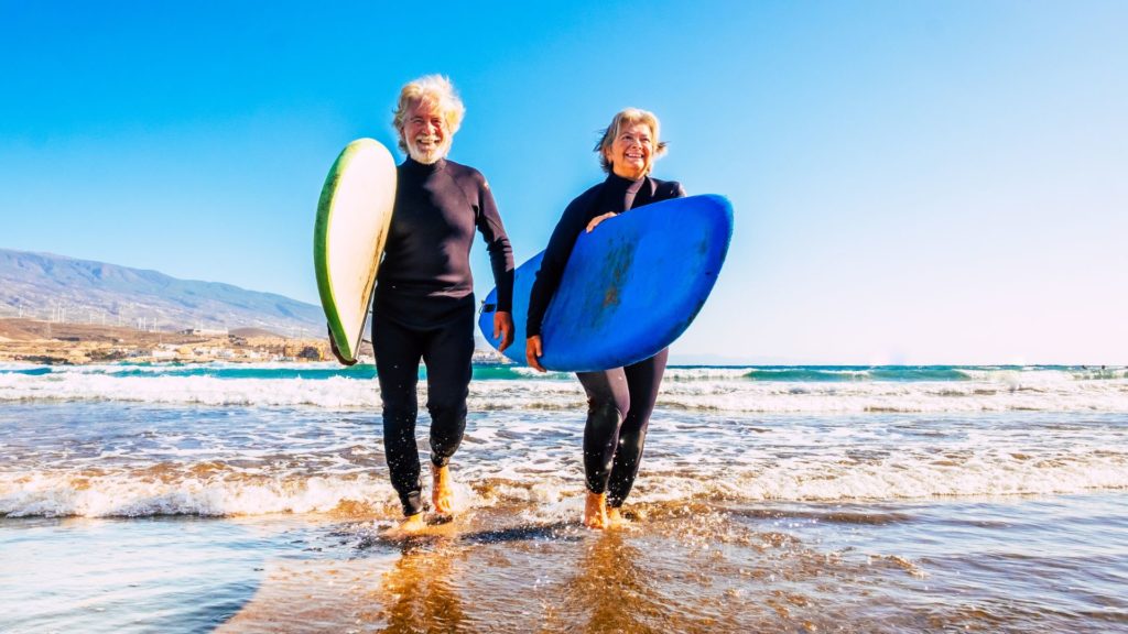 An elderly couple smiling and coming out of the water with surf boards.